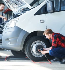 Two young professional car repair technicians serving one of automobiles in hangar or workshop